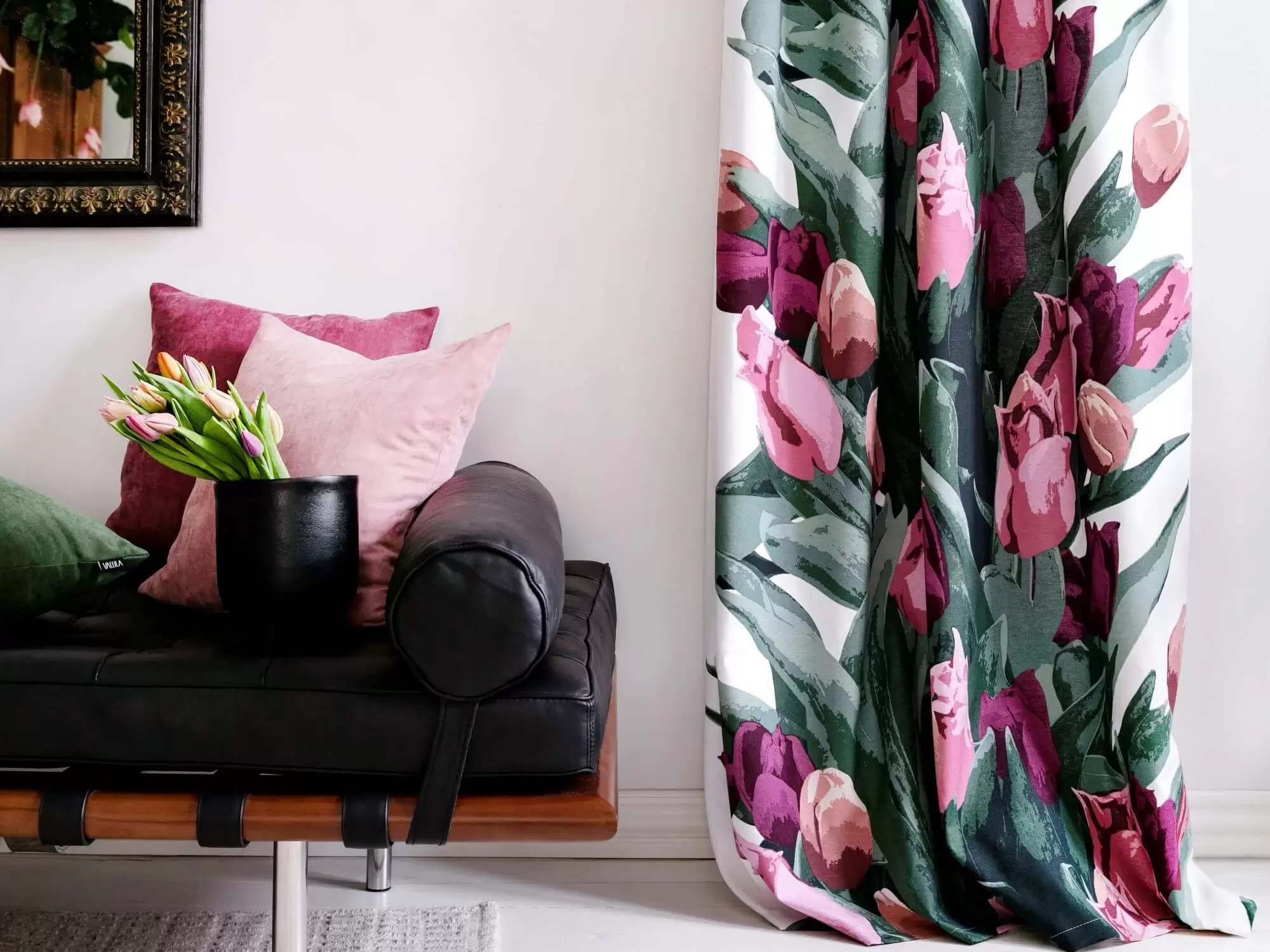 Zasłony do salonu w kwiaty na tle okna i brązowej sofy w skandynawskim salonie. Tulipany w kolorach różowych, amarantowych pięknie prezentują się na tle zielonych liści.