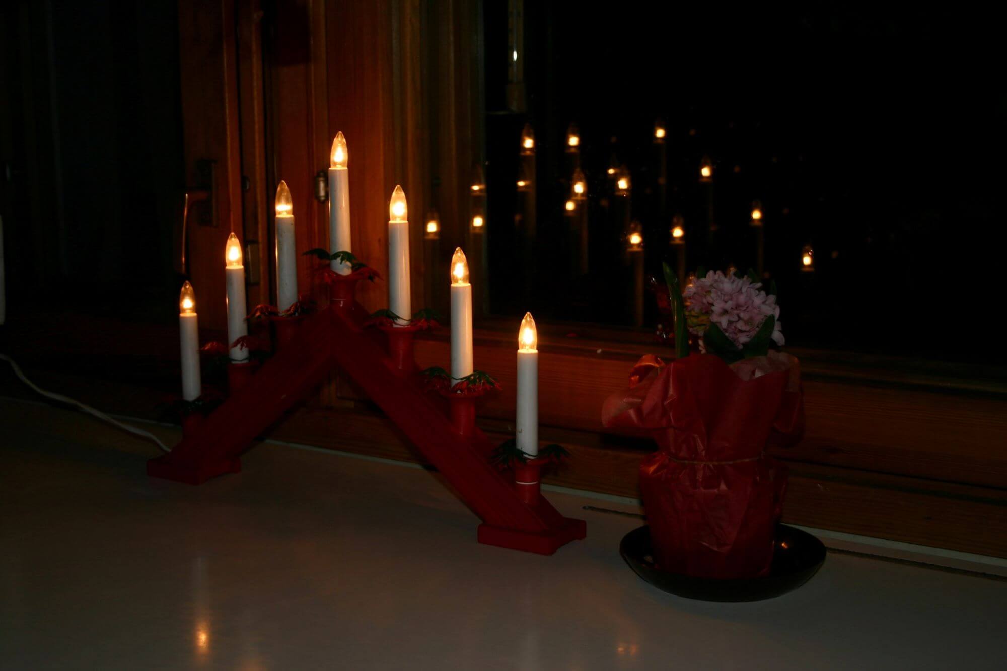 Świąteczna dekoracja okna, czyli drewniany świecznik w kolorze czerwonym postawiony na parapecie okna.