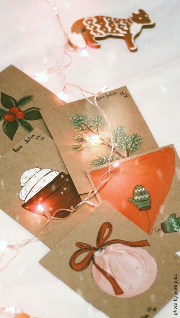 Świąteczne kartki na Boże Narodzenie wykonane własnoręcznie. Na kartkach namalowane są świąteczne akcenty jak bombki, jodłą oraz piernikami.