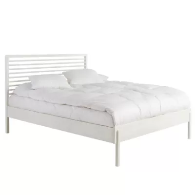 Designerskie łóżko białe LENNU. Widoczne w całości z materacem łóżko białe dwuosobowe z wysokim ażurowym drewnianym szczytem. Na łóżku do sypialni 160x200 na wysokich nóżkach leży biała kołdra i poduszki