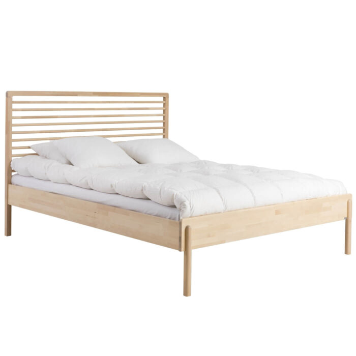 Łóżko design LENNU. Widoczne w całości łóżko 160x200 z wysokim ażurowym drewnianym szczytem. Na łóżku do sypialni na wysokich nóżkach leży materac, kołdra i poduszki
