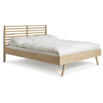 Łóżko drewniane 160x200 NOTTE. Widoczne w całości łóżko z drewna na wysokich nóżkach, z ażurowym zagłówkiem z litego drewna brzozy skandynawskiej i leżąca biała kołdrą. Nowoczesny design
