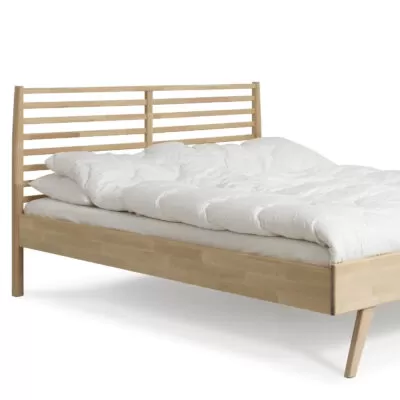 Łóżko drewniane 160x200 NOTTE. Fragment łóżka z drewna brzozy z wysokim ażurowym zagłówkiem i leżącą białą kołdrą. Nowoczesny skandynawski design