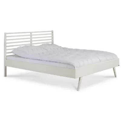 Łóżko drewniane białe 160x200 NOTTE. Widoczne w całości łóżko z drewna na wysokich nóżkach, z ażurowym zagłówkiem z litego drewna brzozy skandynawskiej lakierowanej na kolor biały mat. Na białym łóżku leży biała kołdra. Nowoczesny design