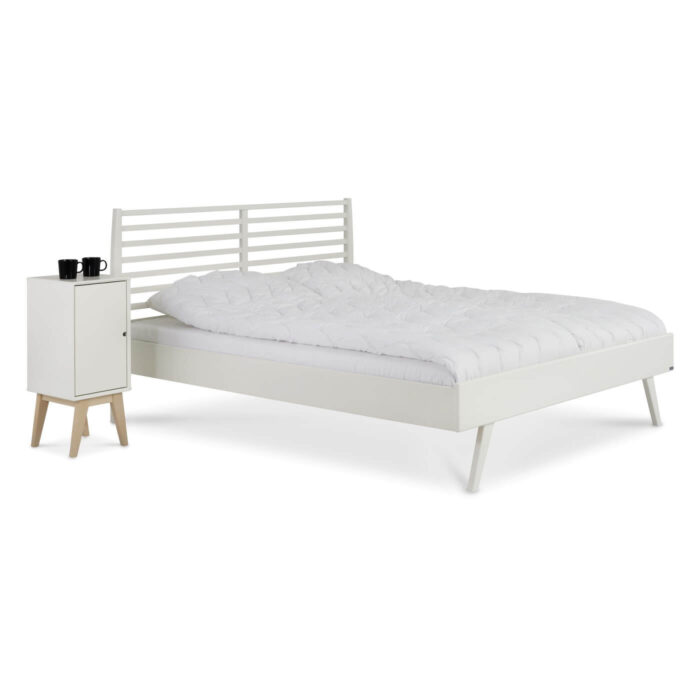 Łóżko drewniane białe 160x200 NOTTE. Łóżko z drewna z wysokim białym ażurowym zagłówkiem i szafka nocna drewniana biała z drzwiczkami stojące obok siebie. Meble na wysokich nóżkach. Nowoczesny skandynawski design