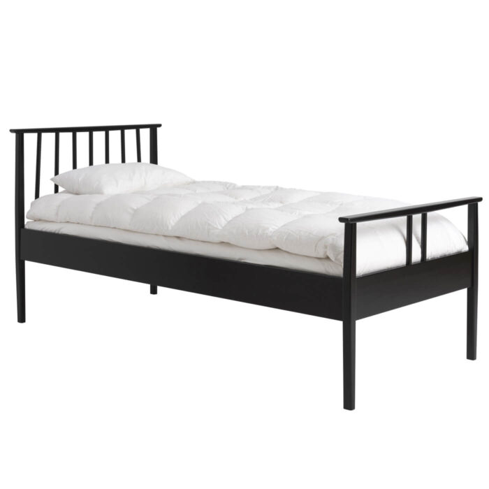 Łóżko drewniane czarne 90x200 NOEL. Łóżko drewniane jednoosobowe widoczne w całości. Na łóżku z pięknym ażurowym szczytem z drewna w kolorze czarnym leży biała kołdra i poduszka. Skandynawski design