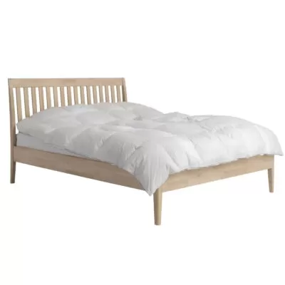Łóżko z drewnianym zagłówkiem MATINEA. Widoczne w całości łóżko drewniane 160x200 z ażurowym drewnianym zagłówkiem, wysokimi nóżkami z litego drewna brzozy skandynawskiej i leżącą białą kołdrą. Nowoczesne wzornictwo