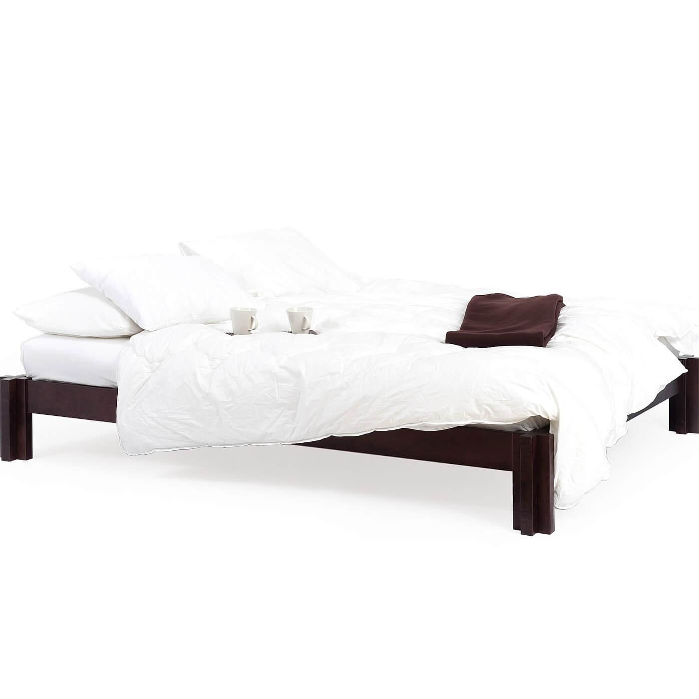 Niskie łóżko wenge MORI 180x200 widoczne w całości. Na łóżku z drewna w kolorze wenge leży materac, biała kołdra, poduszki, brązowy koc i 2 białe kubki. Nowoczesny skandynawski design