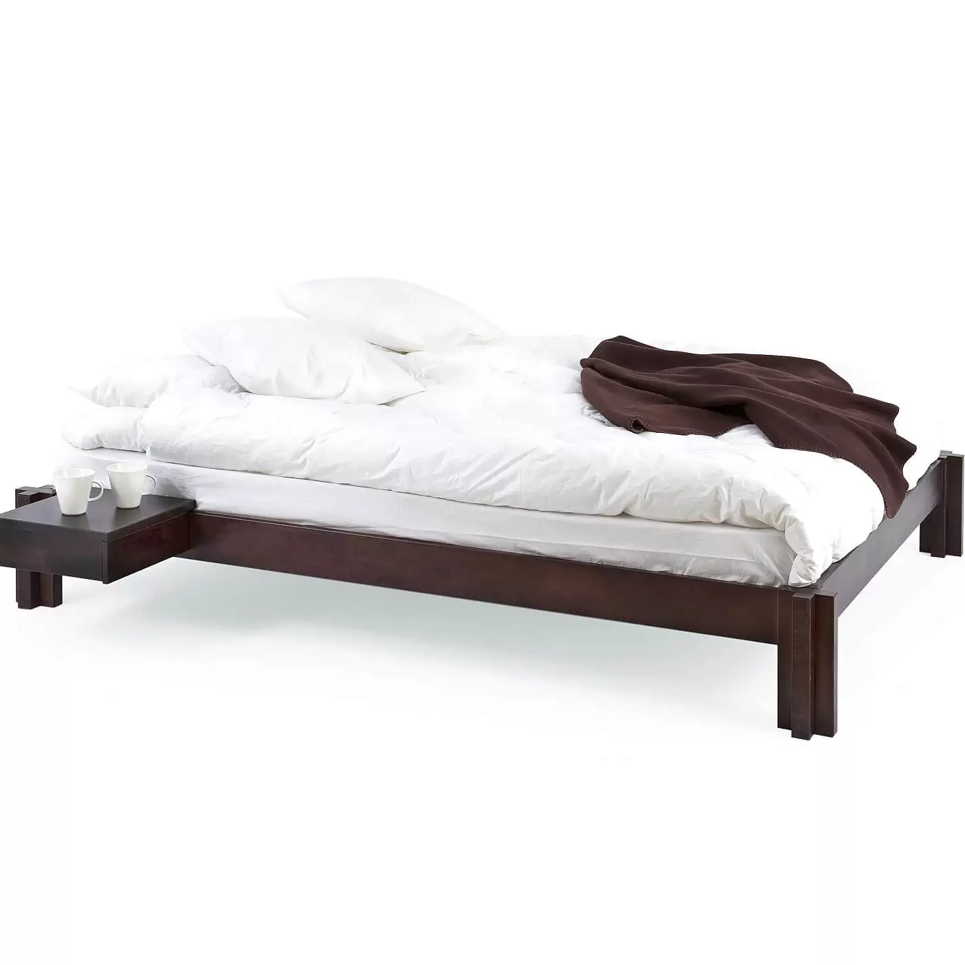 Niskie łóżko wenge MORI. Łóżko nowoczesne na poddasze widoczne w całości. Na łóżku z drewna w kolorze wenge leży materac, biała kołdra, poduszki i koc. Przy łóżku przywieszony stolik nocny wenge z 2 białymi kubkami. Skandynawski design