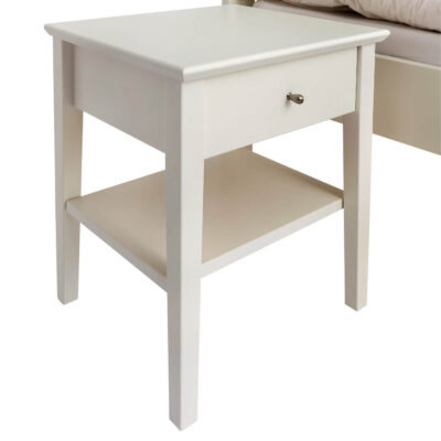 Biały stolik nocny KUUSAMO z drewna brzozy skandynawskiej lakierowany na kolor biały mat widoczny w całości lekko bokiem. Szafka nocna biała z 1 szufladą i 1 białą półką. Skandynawski minimalistyczny design