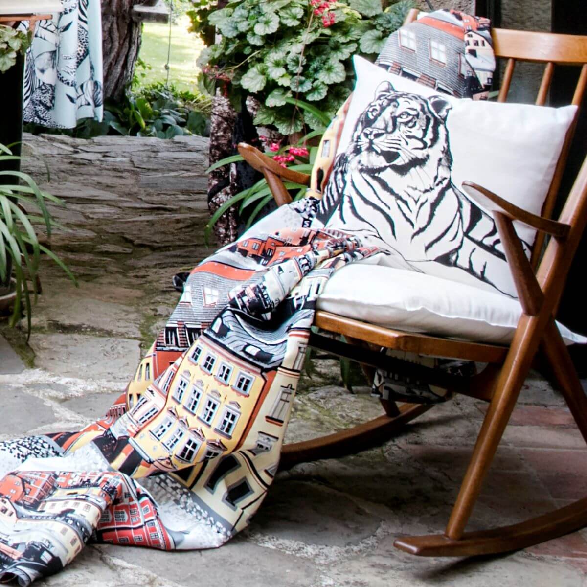 Poszewka dekoracyjna gepard i tygrys SIESTA. Poszewka bawełniana dwustronna na poduszkę z czarną postacią tygrysa leżąca na drewnianym bujanym fotelu