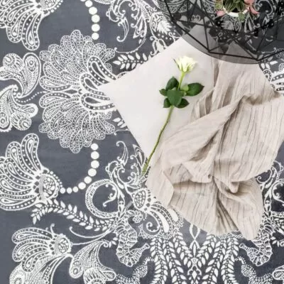 Dywan szaro biały SYVÄMERI. Dekoracyjny szary dywan z białym wzorem w aranżacji z białą różą widoczny we fragmencie. Skandynawski design