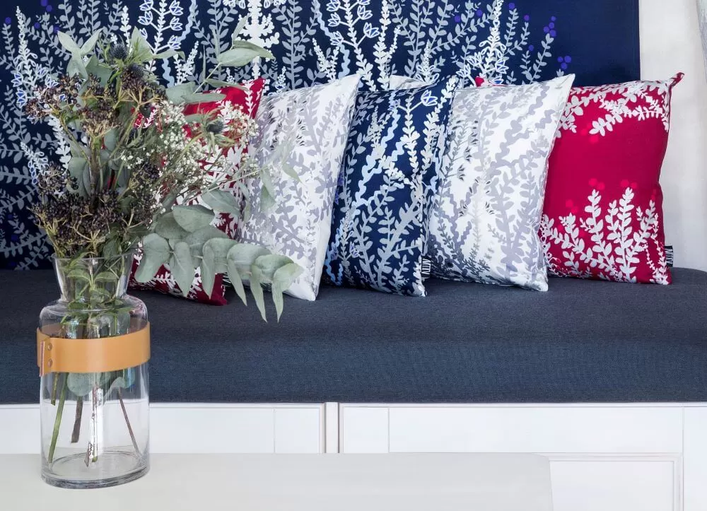 Poszewka dekoracyjna VARVIKKO czerwona granatowa biała aranżacja. Wypełnione bawełniane poszewki dekoracyjne z srebrno szaro i białym wzorem roślin w kolorach czerwonym, granatowym i białym w aranżacji obok siebie. Skandynawski design