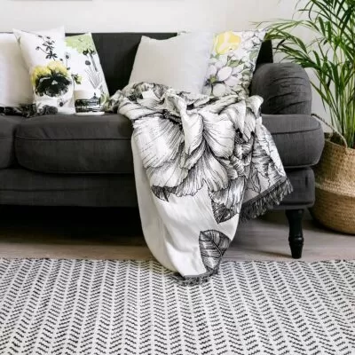 Dywan wełniany KAMPA. Biało czarny wełniany dywan wzór jodełka w aranżacji w salonie obok szarej sofy z poduszkami w kwiaty
