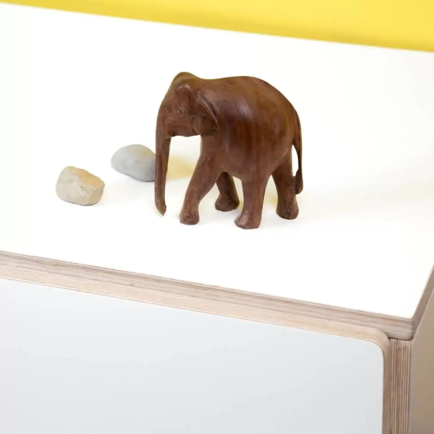 Biały laminat na sklejce fragment mebla firmy RADIS z 2 kamykami i brązową drewnianą figurką słonia